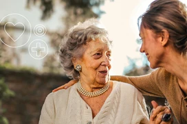 An elderly woman and a younger woman share a joyful moment outdoors.