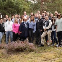 Gruppfoto av leende personer på Epinova, i skogsområde med tallar och ljung.
