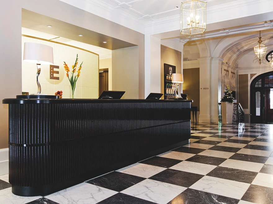 Reception i en elegant hotellobby med marmorgolv, en mörk disk, blommor och taklampor i en klassisk inredning