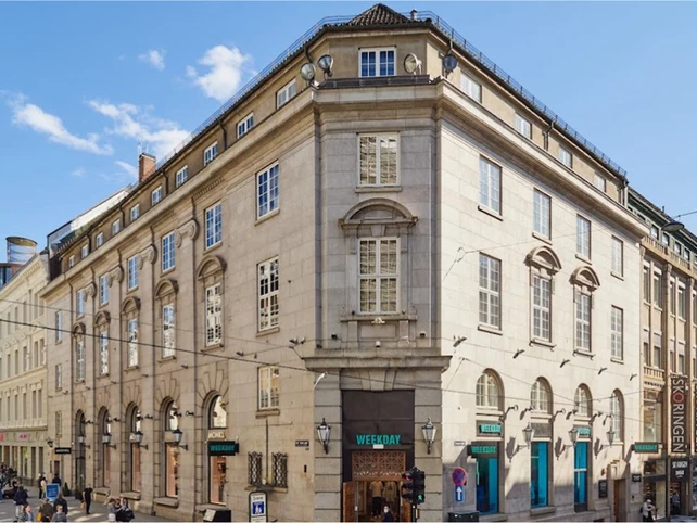 Stadsmiljö med historisk byggnad, blå himmel och butiker, inklusive Weekday, i centrala Stockholm