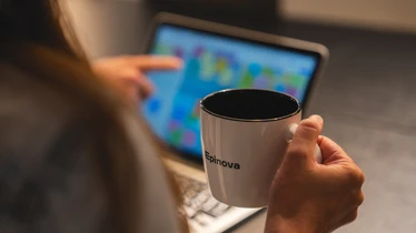 En hand som håller i en kaffekopp framför en laptopskärm