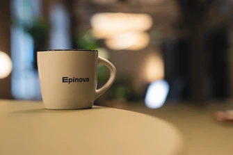 White mug with "Epinova" logo on a table in a softly blurred office