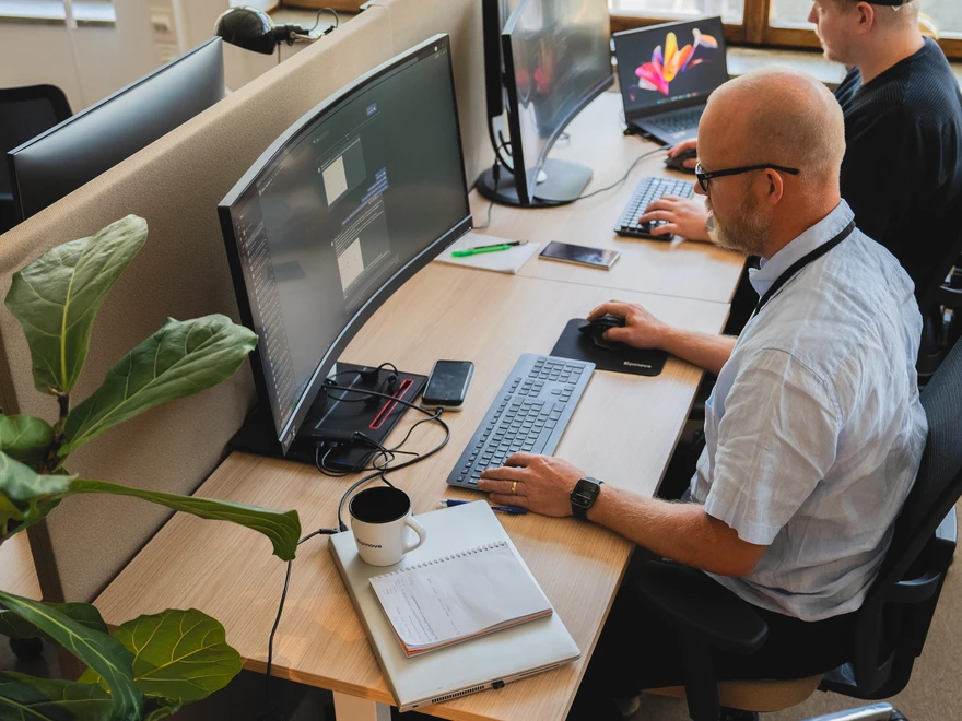Två personer som arbetar vid ett skrivbord med stora datorskärmar