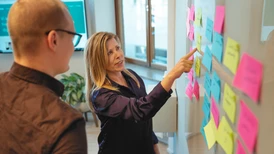 Två personer arbetar vid whiteboard-tavla med postit-lappar