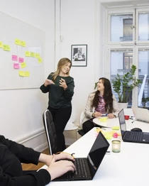 Personer i ett möte i konferensrum diskuterar framför en whiteboard med klisterlappar. 
