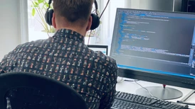 Man sitter vid skrivbord och programmerar på en stor datorskärm. 