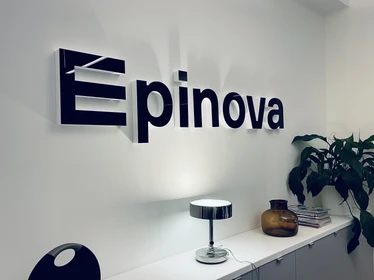 Epinova-logotyp på kontorsvägg med modern inredning, inklusive en lampa och växter