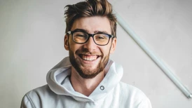 Leende man med glasögon och skäggklädd i vit hoodie
